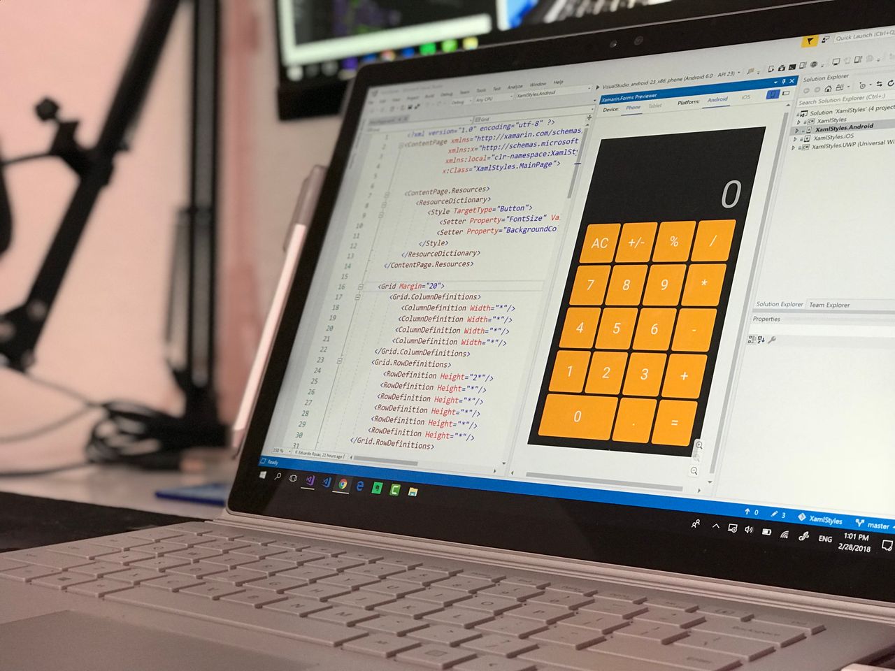 team-01 A laptop screen shows a coding application with a calculator design in a tech office setting.